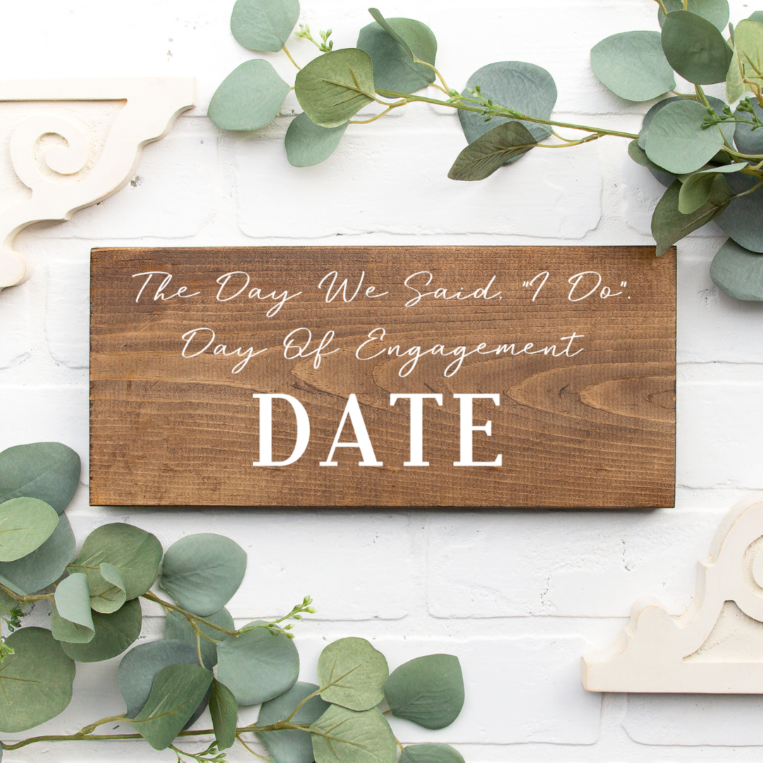 Wooden sign with wedding date text on a white background with greenery