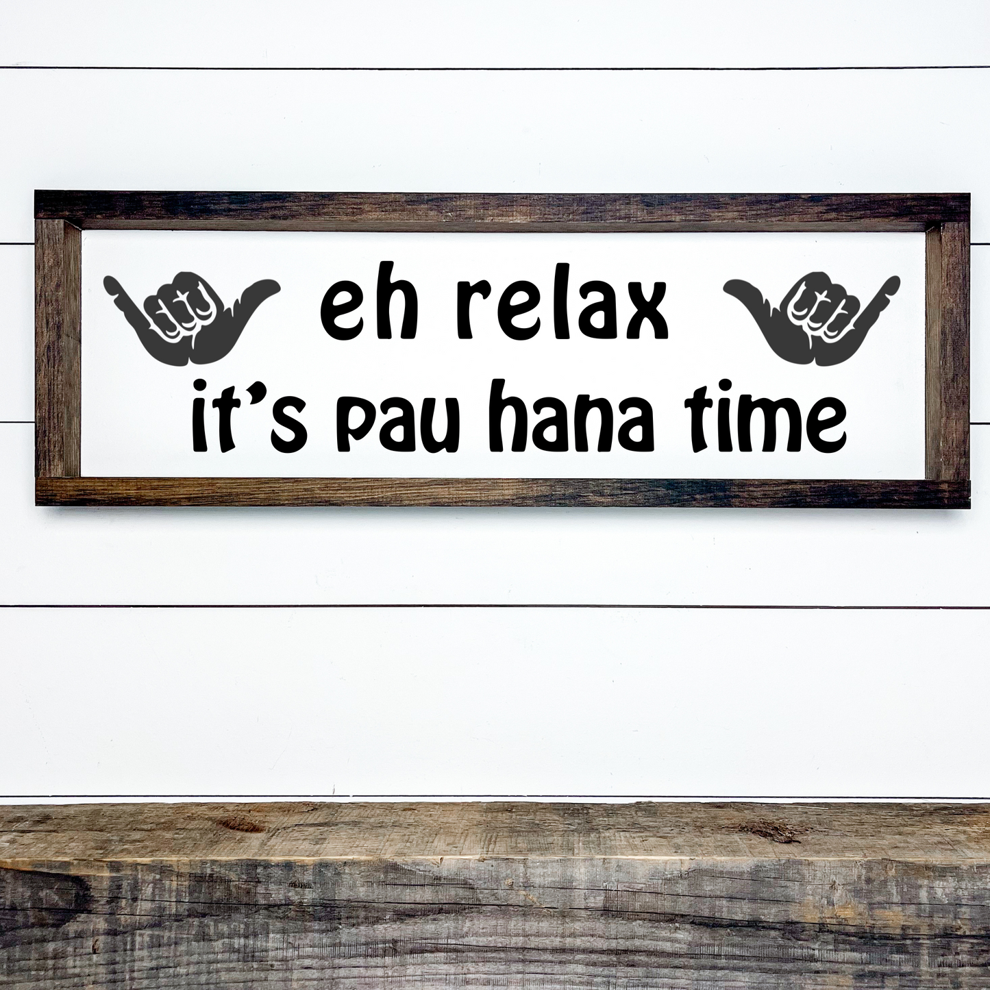 Framed wood sign with island font text “Eh Relax It’s Pau Hana Time,” shown hanging in a tropical home bar or kitchen setting.