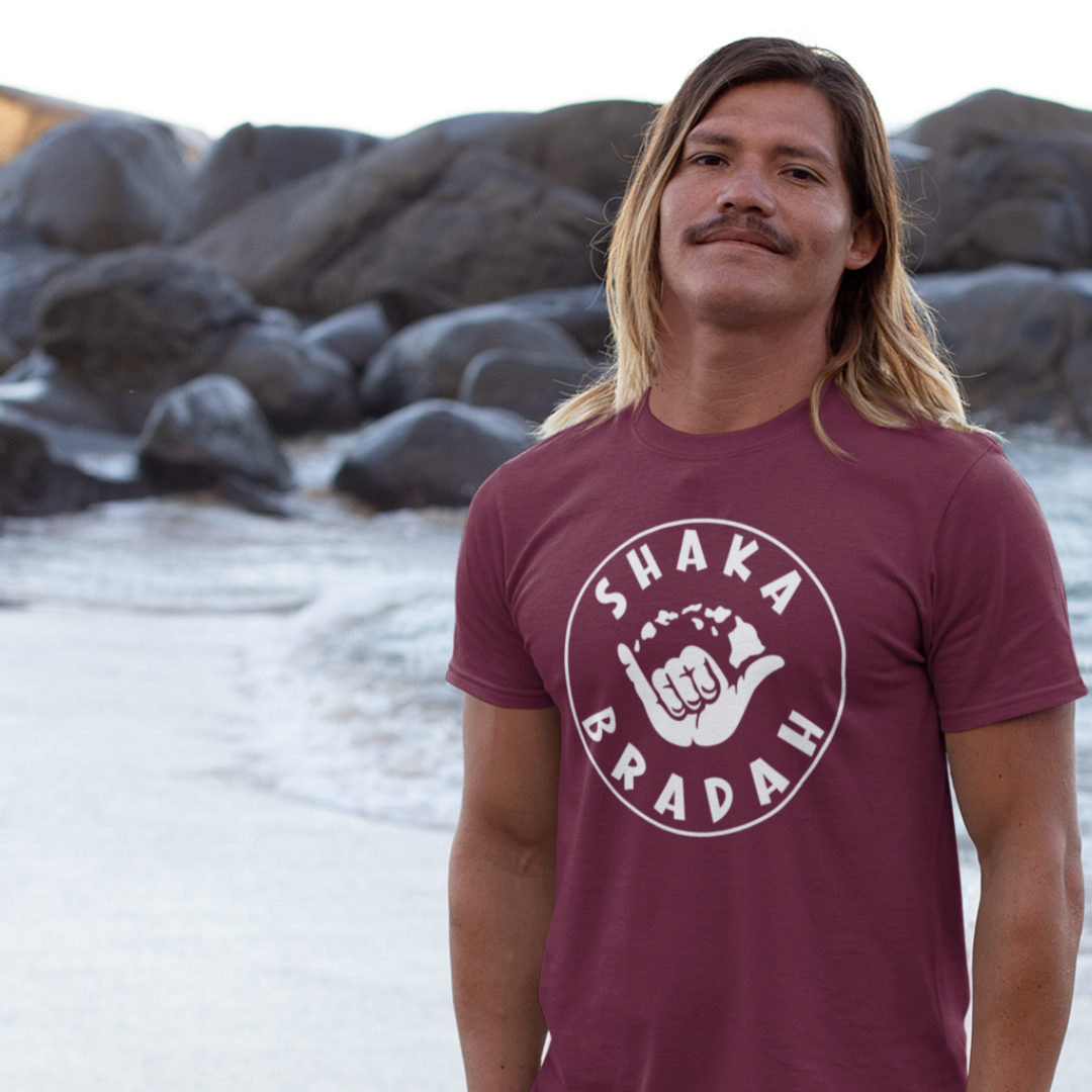 A man wearing a men's t-shirt that says "Shaka Bradah" in a simple white font with a graphic of a hand making the shaka sign.