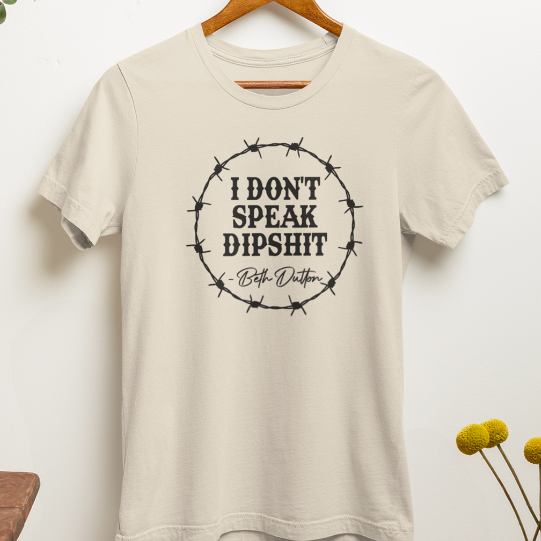 "I Don't Speak Dipshit" t-shirt hanging on a hanger, a funny Western-inspired shirt.