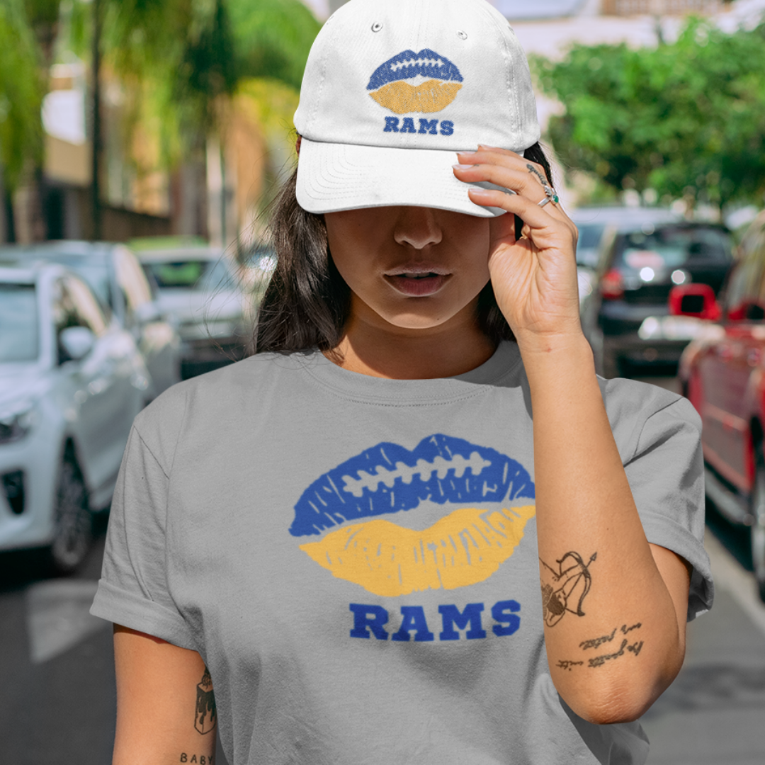 A woman wearing football game day t-shirt in grey color with a lip-themed design in blue and yellow on top and the team name Rams written below.