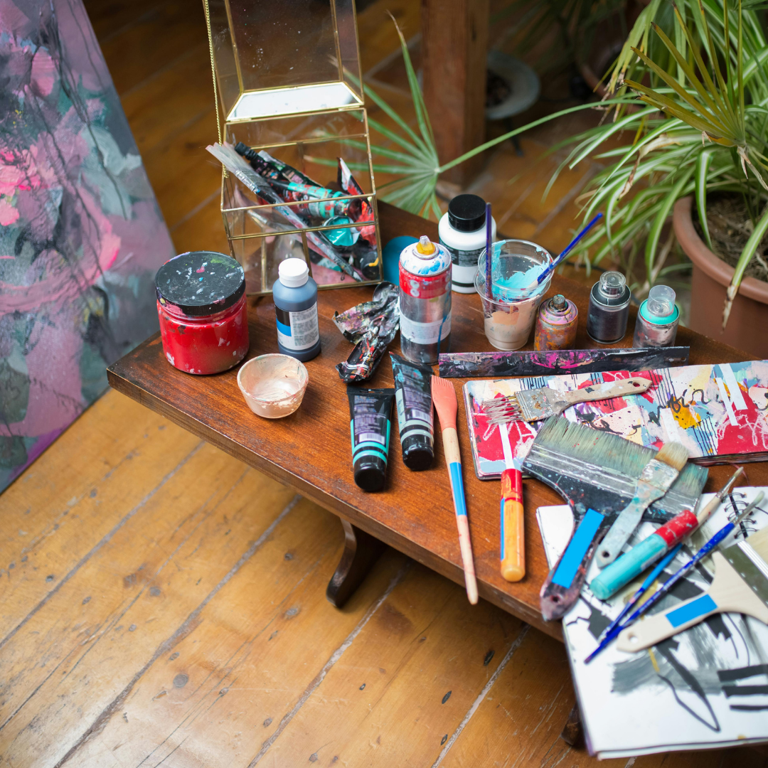 Art supplies including paint bottles, brushes, and canvases on a wooden table.