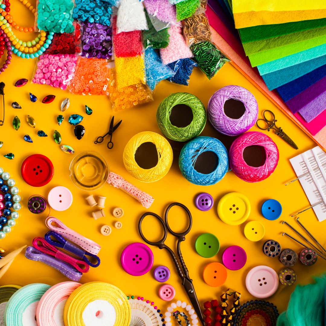 Colorful assortment of craft supplies including yarn, buttons, scissors, and ribbons on a yellow background.