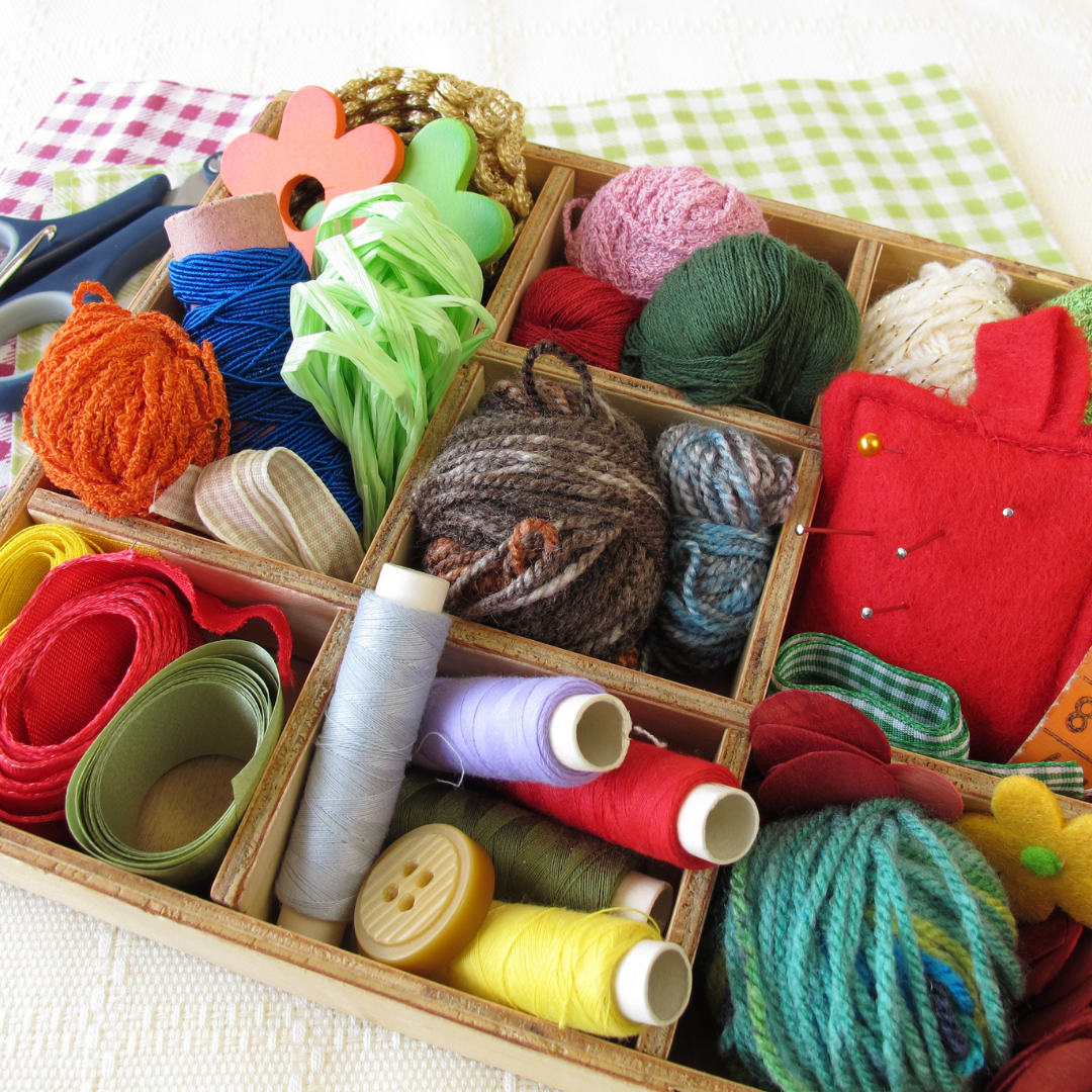 Colorful yarn and thread spools in a wooden box on a checkered tablecloth.