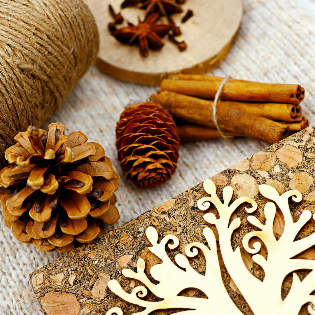 Wooden decorative piece with intricate carvings, cinnamon sticks, pine cones, and twine on a textured surface.