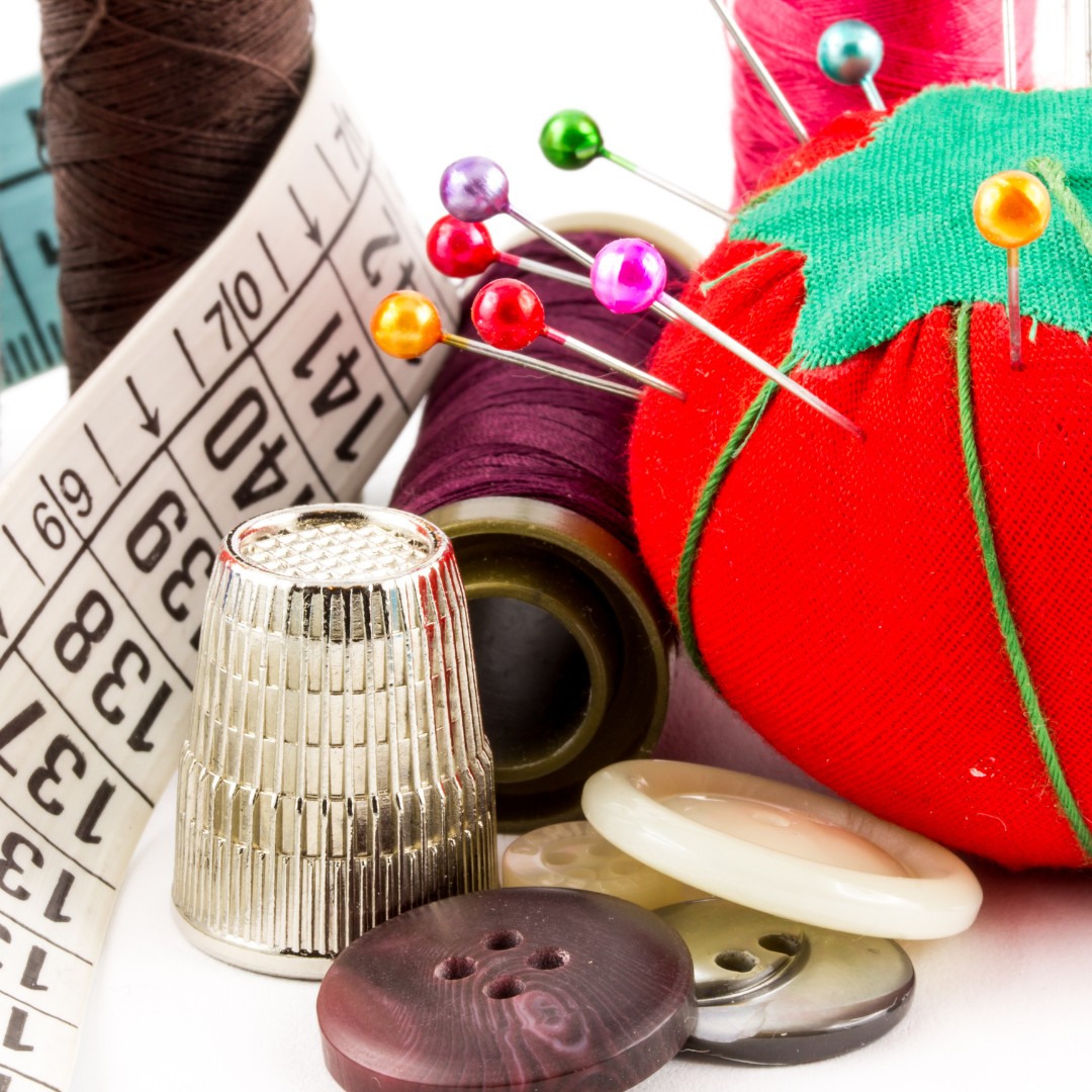 Assorted sewing items including thread, pins, a thimble, and buttons on a white background.