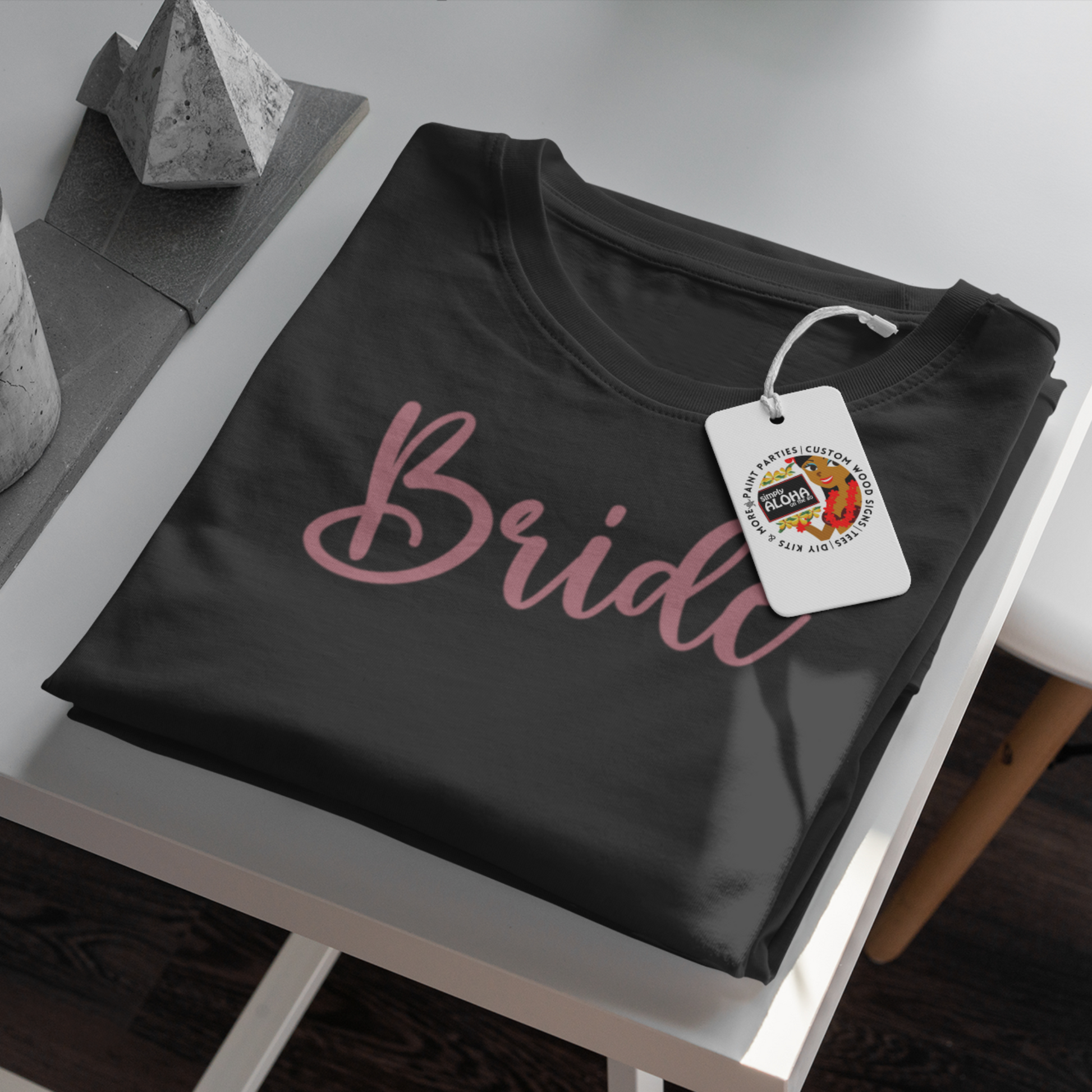 A closeup look of a clean and chic black t-shirt with the word "Bride" printed in a subtle, elegant white font. The shirt is a must-have for a bridal shower or bachelorette party
