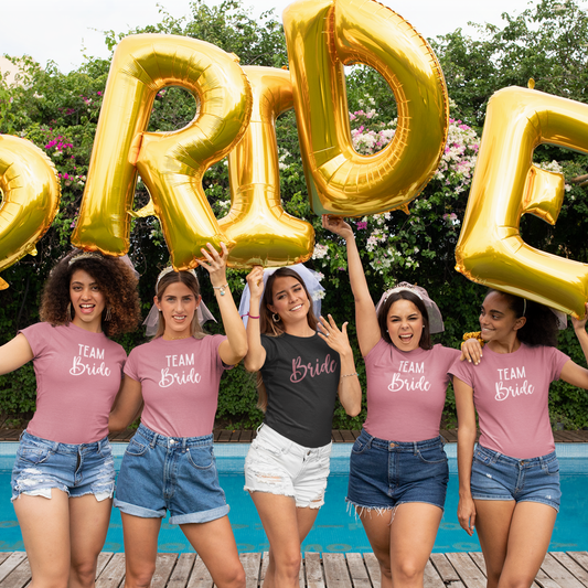 A group of the bridal tribe in the backyard pool wearing Bride Tribe & Team Bride T-Shirts – Bachelorette Party T-shirts in pink and black – Simply Aloha On The Go