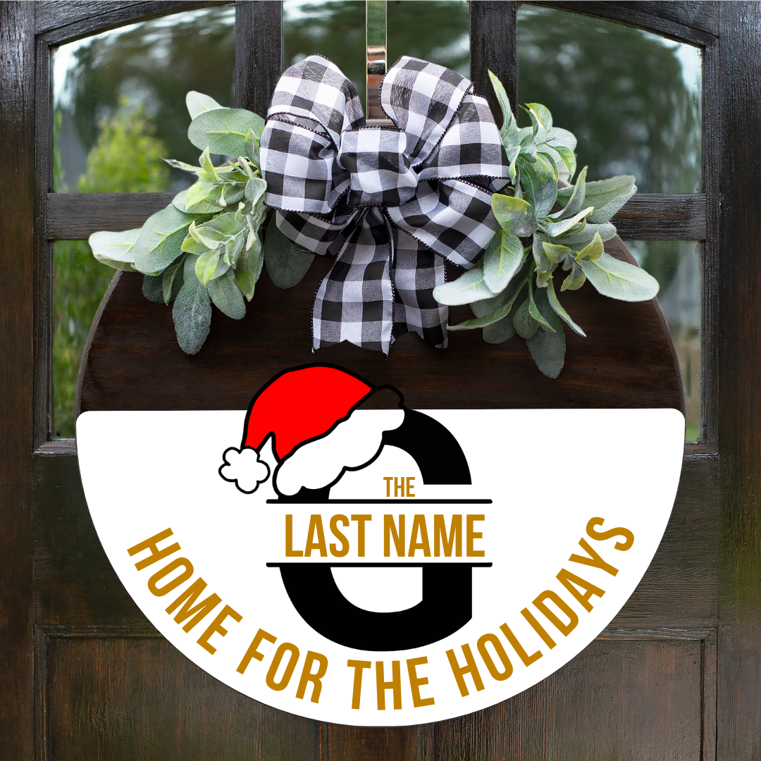 Personalized round wooden Home for the Holidays monogram door sign featuring a large black letter G with a Santa hat and gold text accents