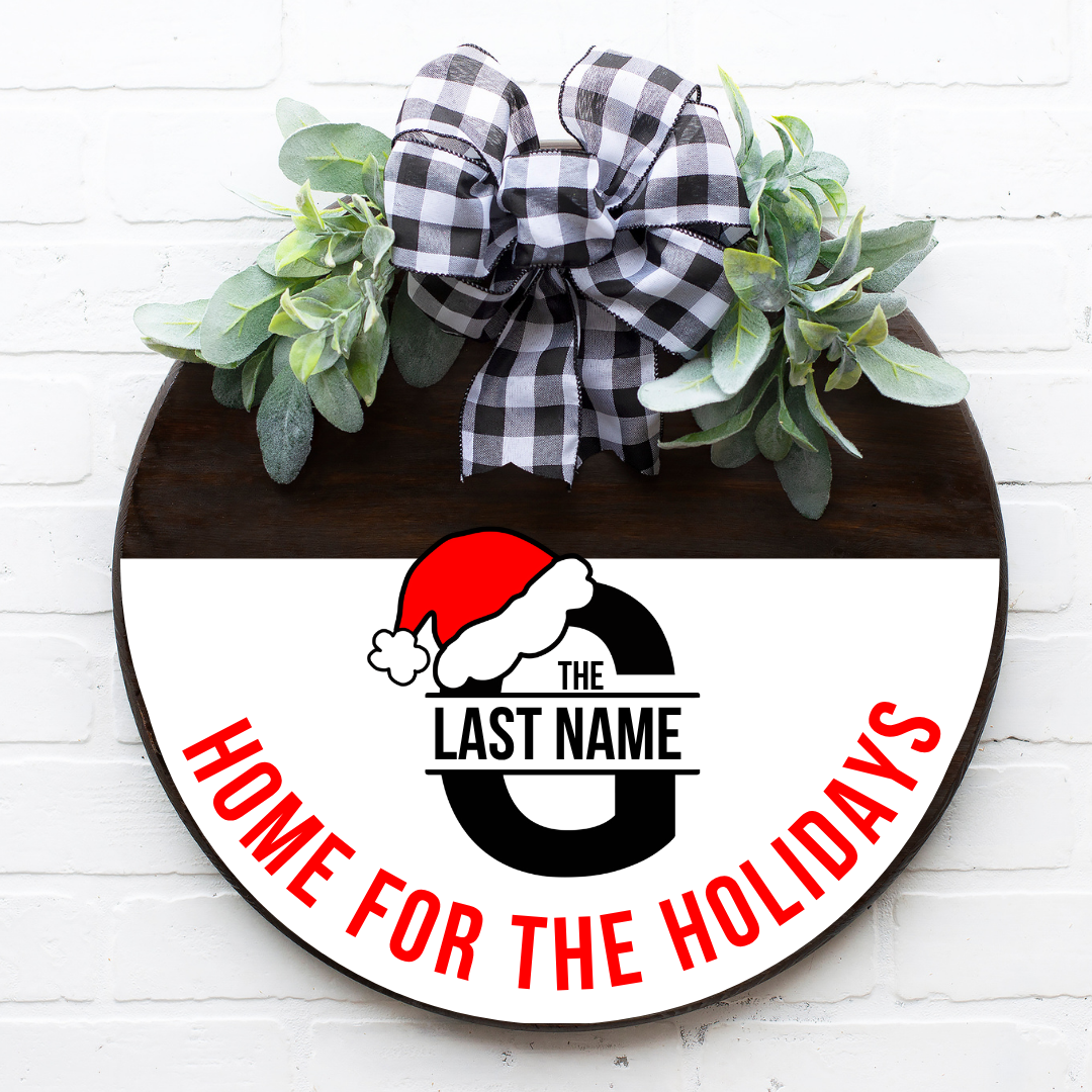 Personalized round wooden Home for the Holidays monogram door sign featuring a large black letter G with a Santa hat and red text accents.