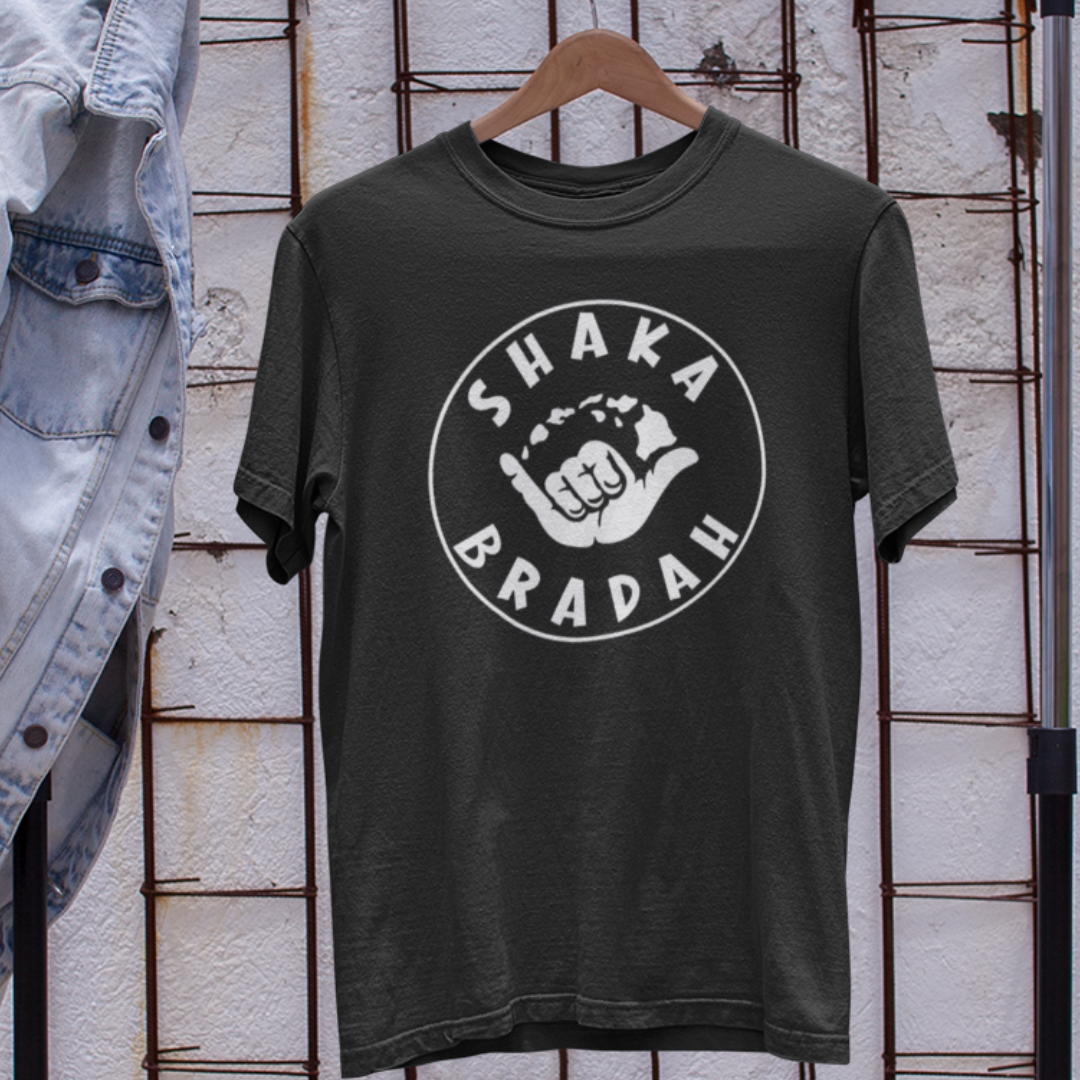 Shaka Bradah T-Shirt on a hanger in black, white font with a graphic of a hand making the shaka sign..