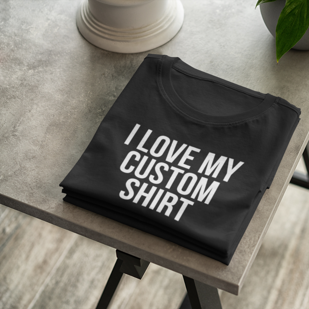 A flat-lay view of a black custom personalized t-shirt displaying a bold white text graphic that reads I Love My Custom Shirt.