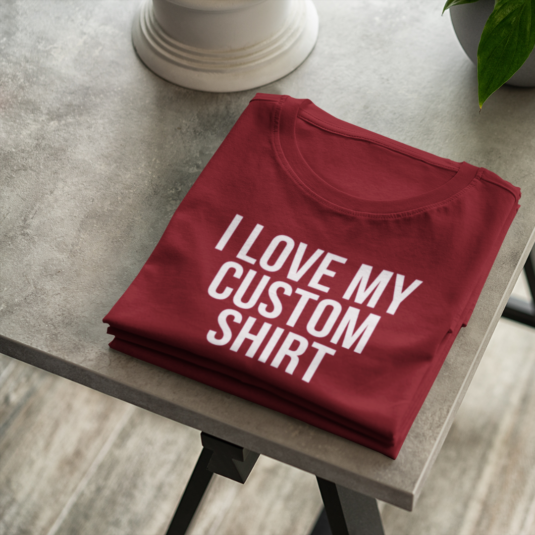 A flat-lay view of a maroon custom personalized t-shirt displaying a bold white text graphic that reads I Love My Custom Shirt.