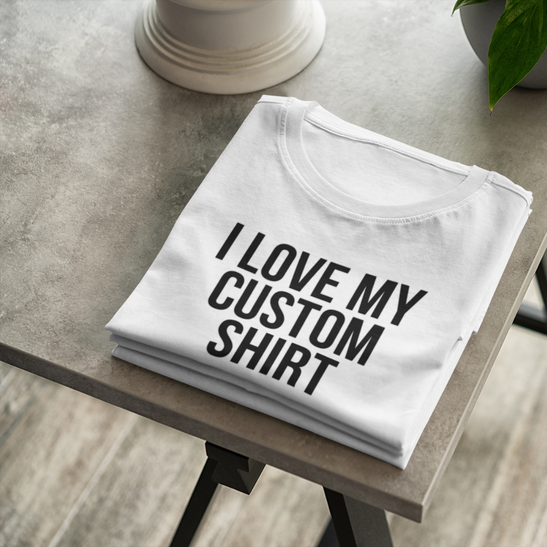 A flat-lay view of a white custom personalized t-shirt displaying a bold black text graphic that reads I Love My Custom Shirt.