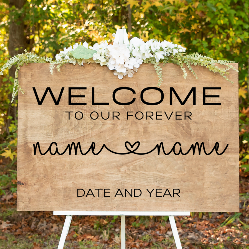 A custom, double-sided wedding welcome sign propped on an easel. The front side features the couple's names and a wedding date, while a blurred image hints at a different design on the back.