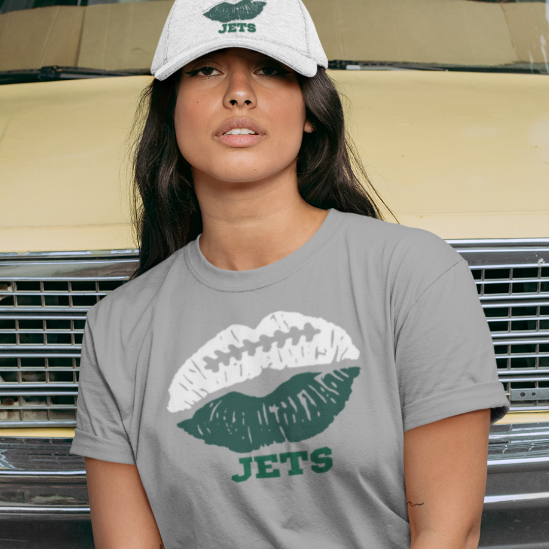 A woman wearing football game day t-shirt in grey color with a lip-themed design in green and white on top and the team name Jets written below.
