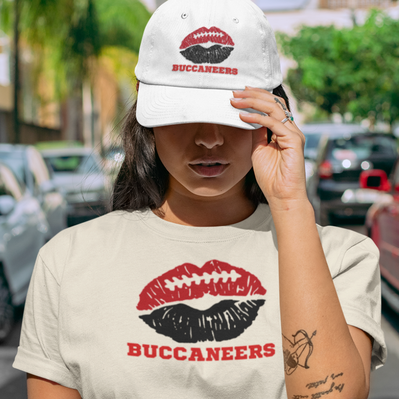 A woman wearing game day t-shirt in sand color with a lip-themed design in red and black on top and the team name Buccaneers written below.
