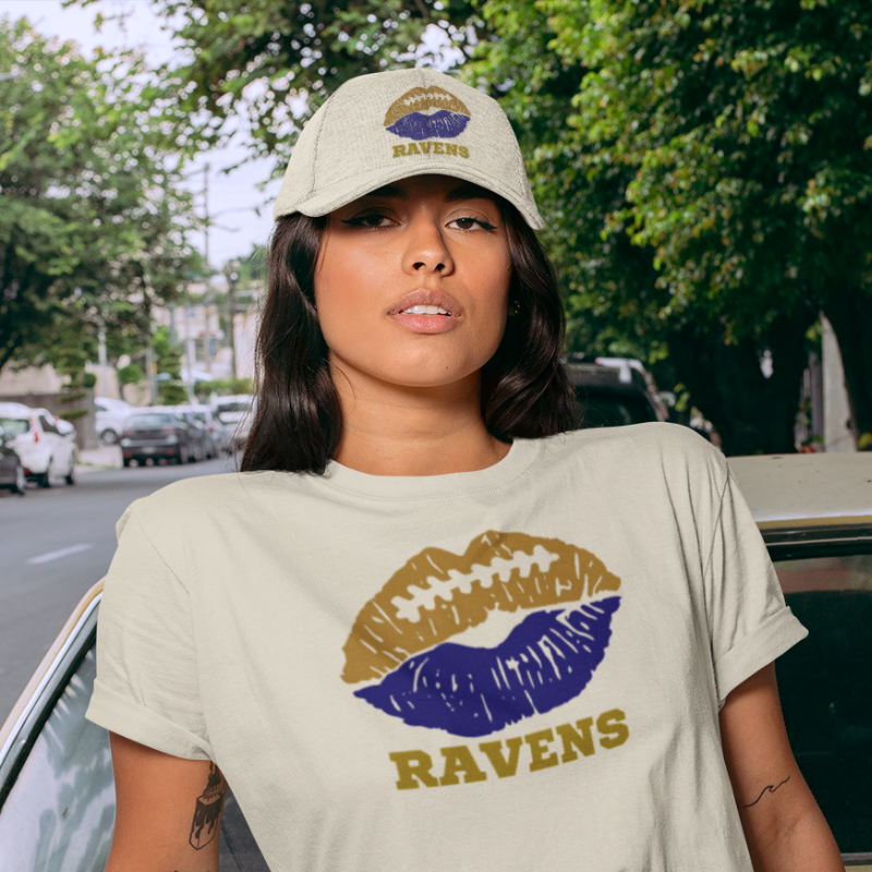 A woman wearing game day t-shirt in white color with a lip-themed design in purple and white gold on top and the team name written below. 