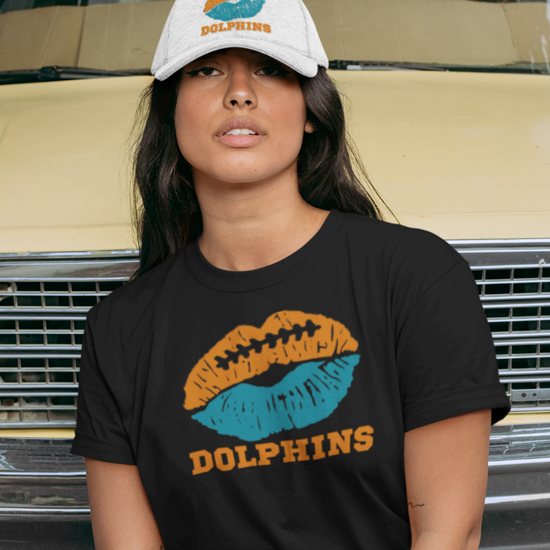 A woman wearing football game day t-shirt in black color with a lip-themed design in orange and aqua on top and the team name Dolphins written below.