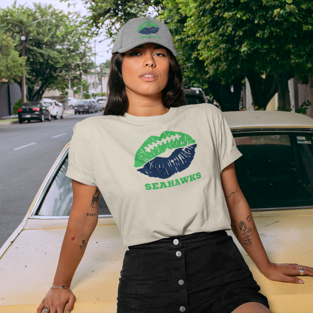 A woman wearing football game day t-shirt in cream color with a lip-themed design in blue and green on top and the team name Seahawks written below.