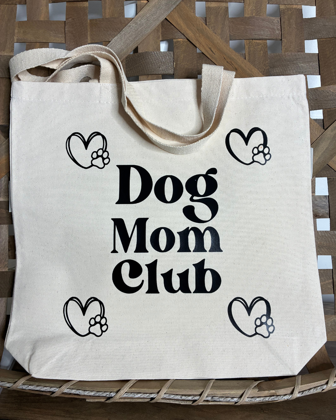 Cream organic cotton tote bag with "Dog Mom Club" in black serif text, surrounded by four heart icons with paw prints inside.