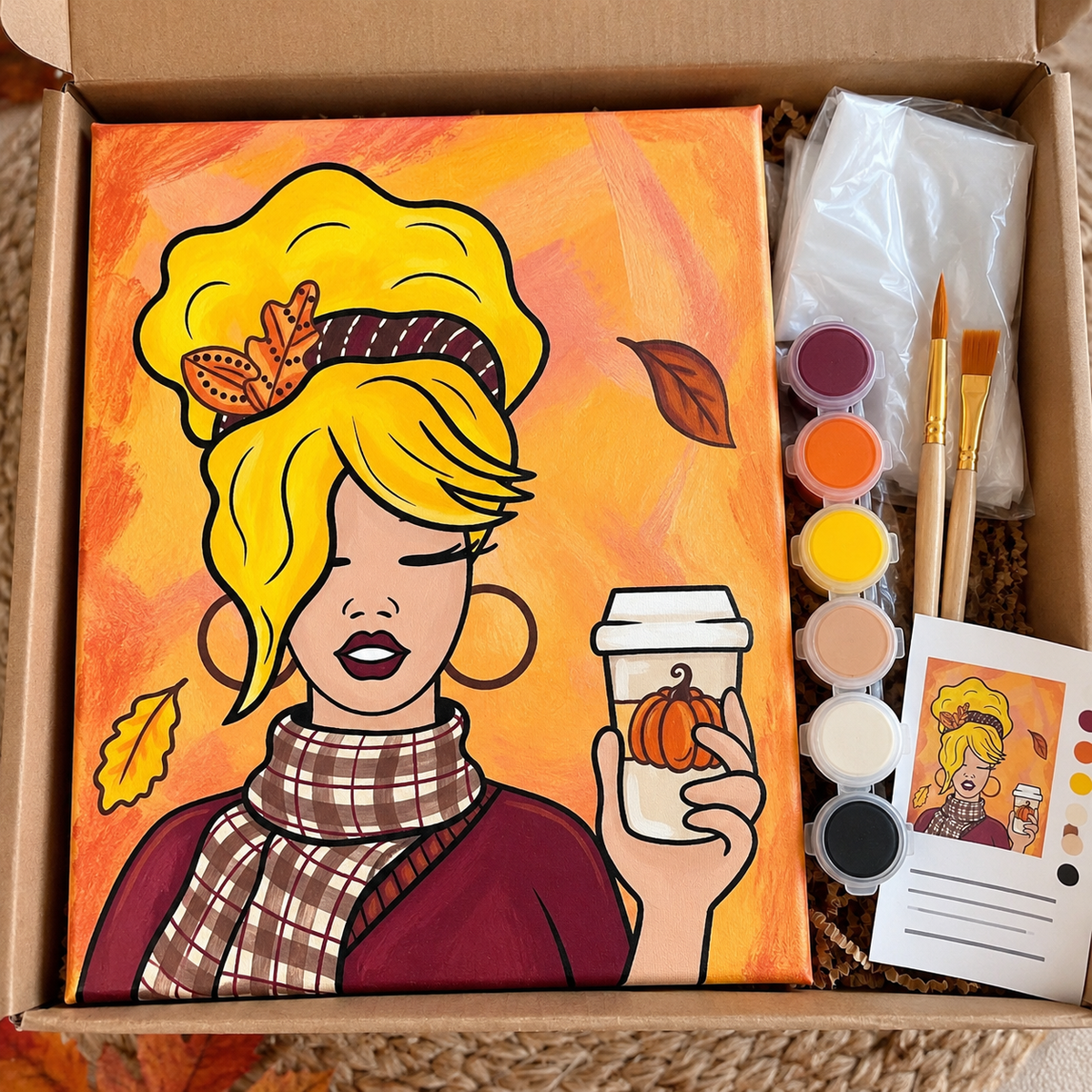 Fall DIY paint kit displayed in a plain kraft box with pumpkin spice girl canvas design, acrylic paints, paintbrushes, disposable apron, and instructions.