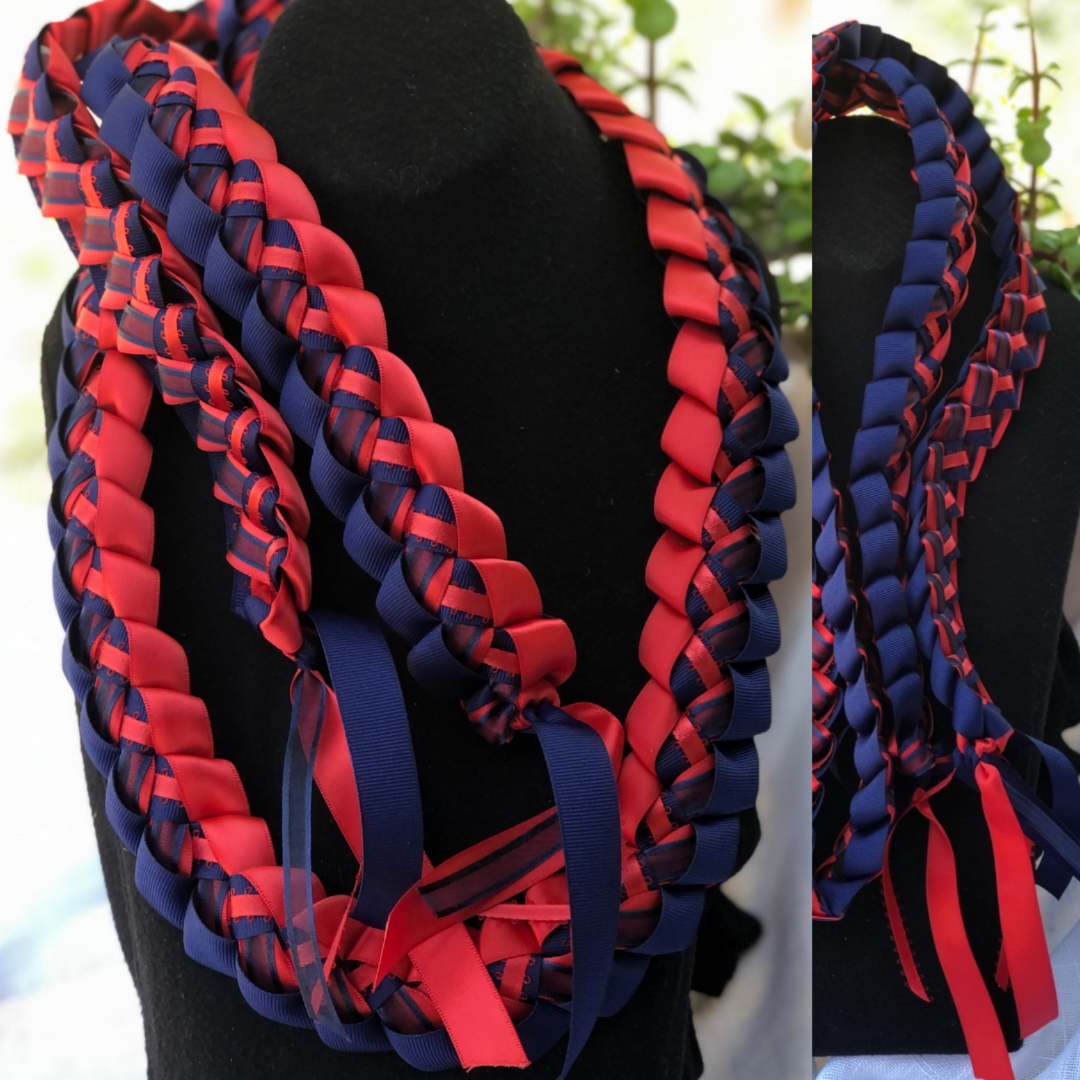 Personalized graduation lei in red and navy blue school colors showing braided ribbon patterns and tassel details on a black stand.