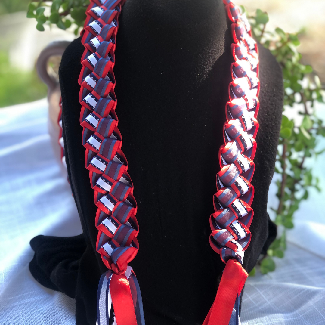 Graduation Leis 2027 collection featuring handcrafted red, white and blue braided backside ribbon lei displayed on black stands for graduation celebrations.