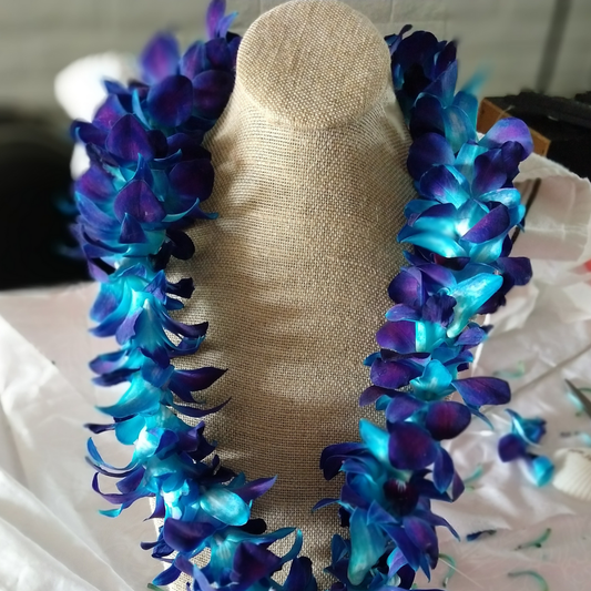 Orchid lei with turquoise blue and deep purple flowers displayed on a beige stand, hand-strung for graduation and wedding celebrations in Arizona.