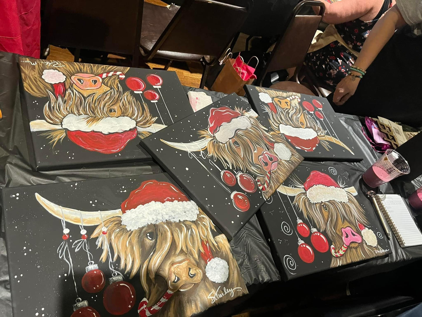 Paintings of a highland cow wearing a Santa hat on black backgrounds.