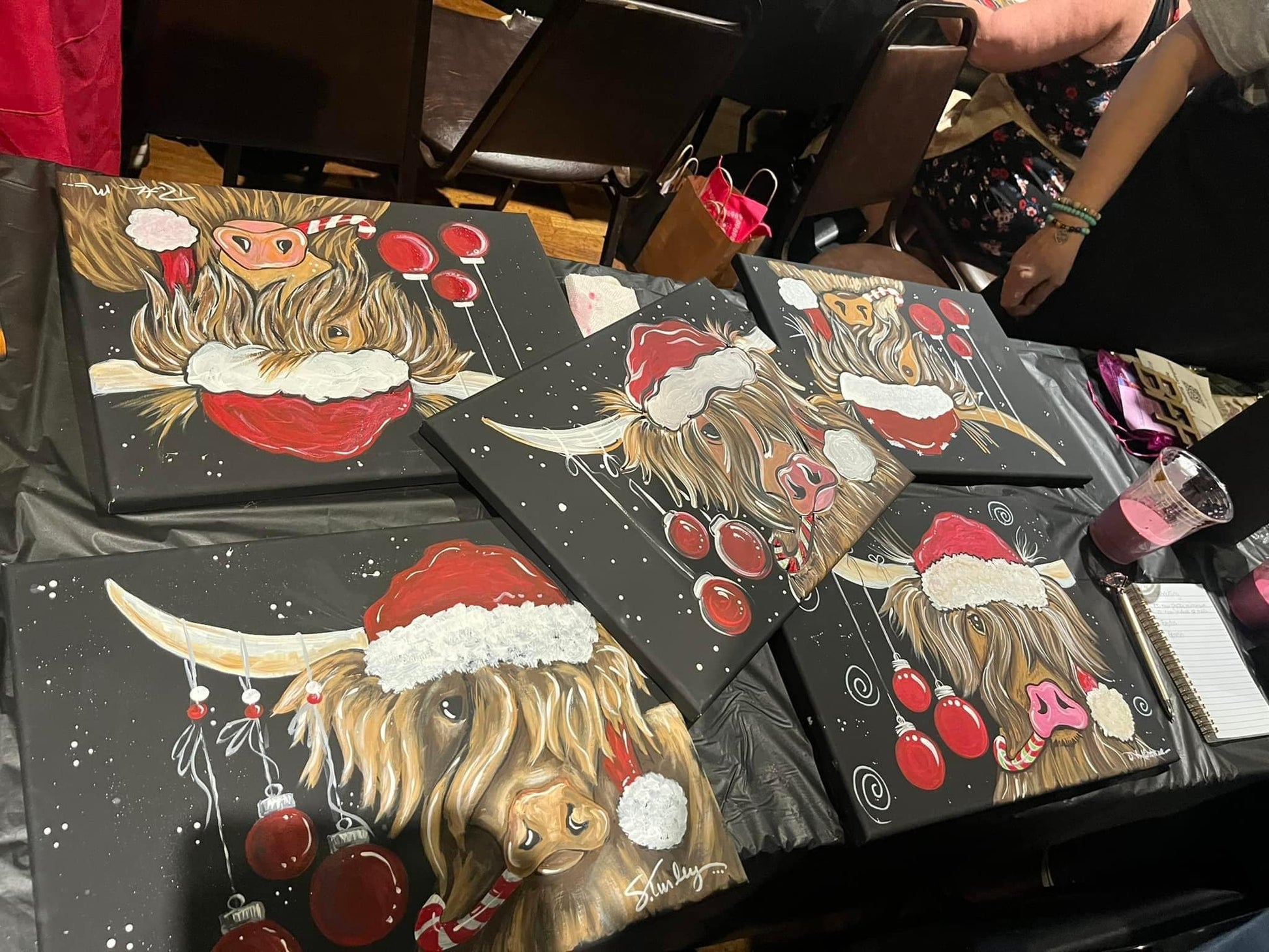 Paintings of a highland cow wearing a Santa hat on black backgrounds.