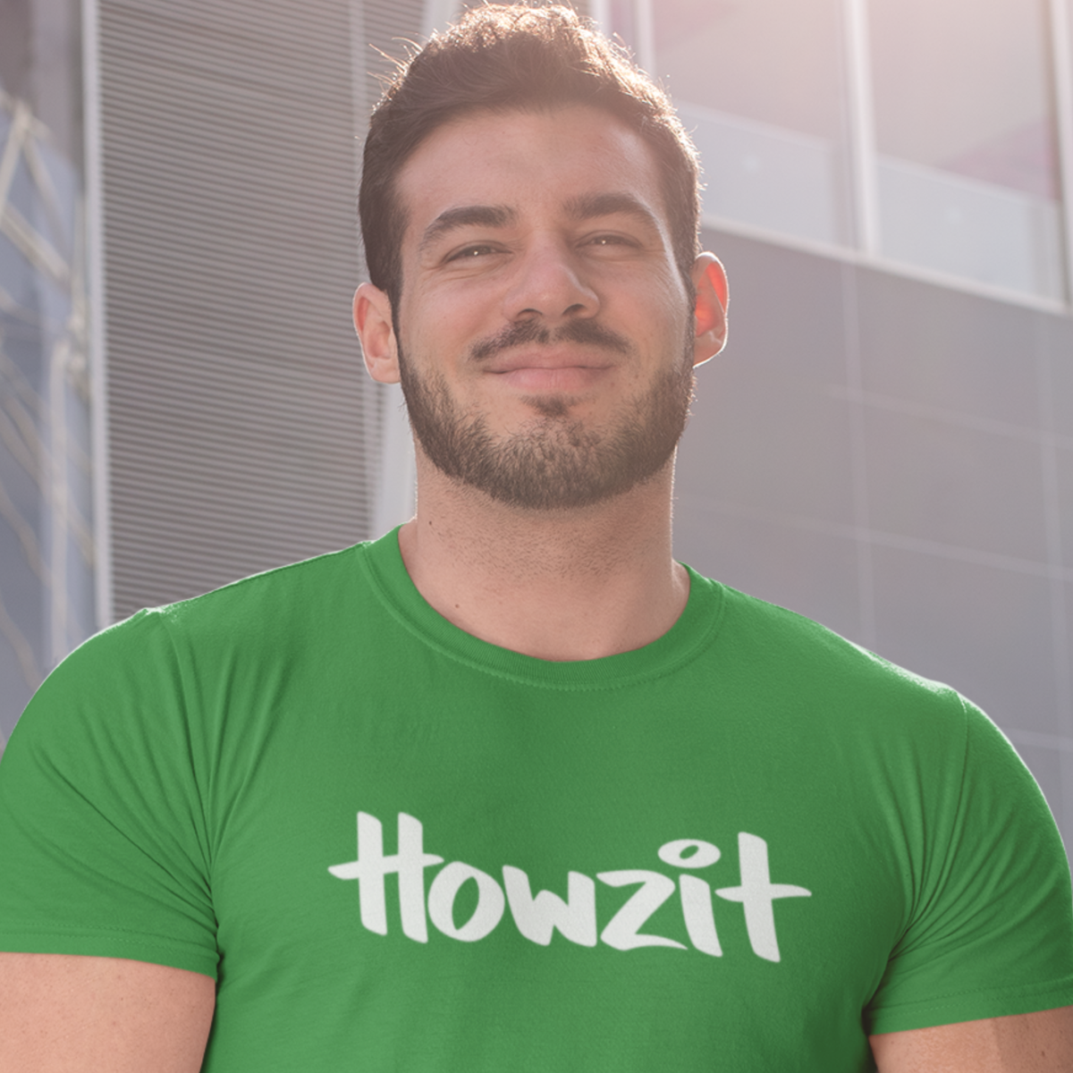 A man wearing a green men's t-shirt that says "Howzit" in a simple white font, a Hawaiian slang shirt. Available in different sizes and colors.