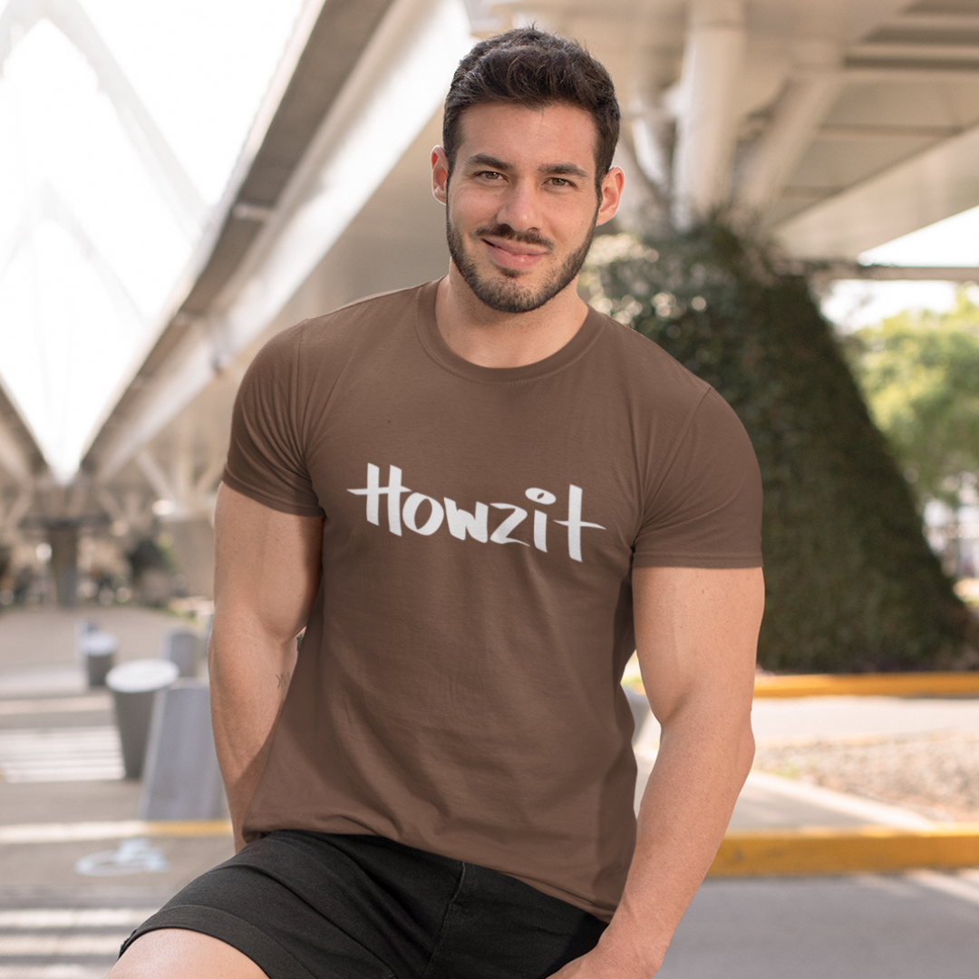 A man wearing a brown men's t-shirt that says "Howzit" in a simple white font, a Hawaiian slang shirt.