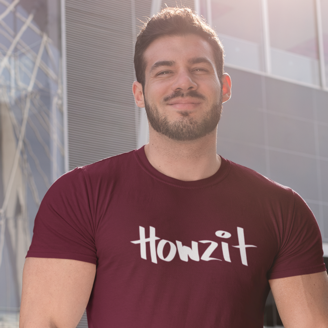 A man wearing a red men's t-shirt that says "Howzit" in a simple white font, a Hawaiian slang shirt.