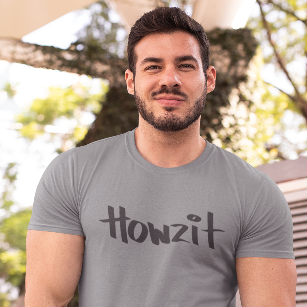 A man wearing a grey men's t-shirt that says "Howzit" in a simple white font, a Hawaiian slang shirt. Available in different sizes and colors.
