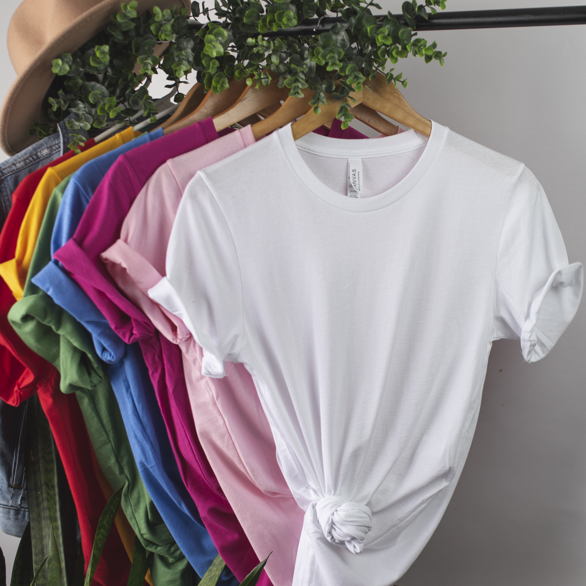 Display of blank women's T-shirts in white, pink, blue, green and other colors on a clothing rack.