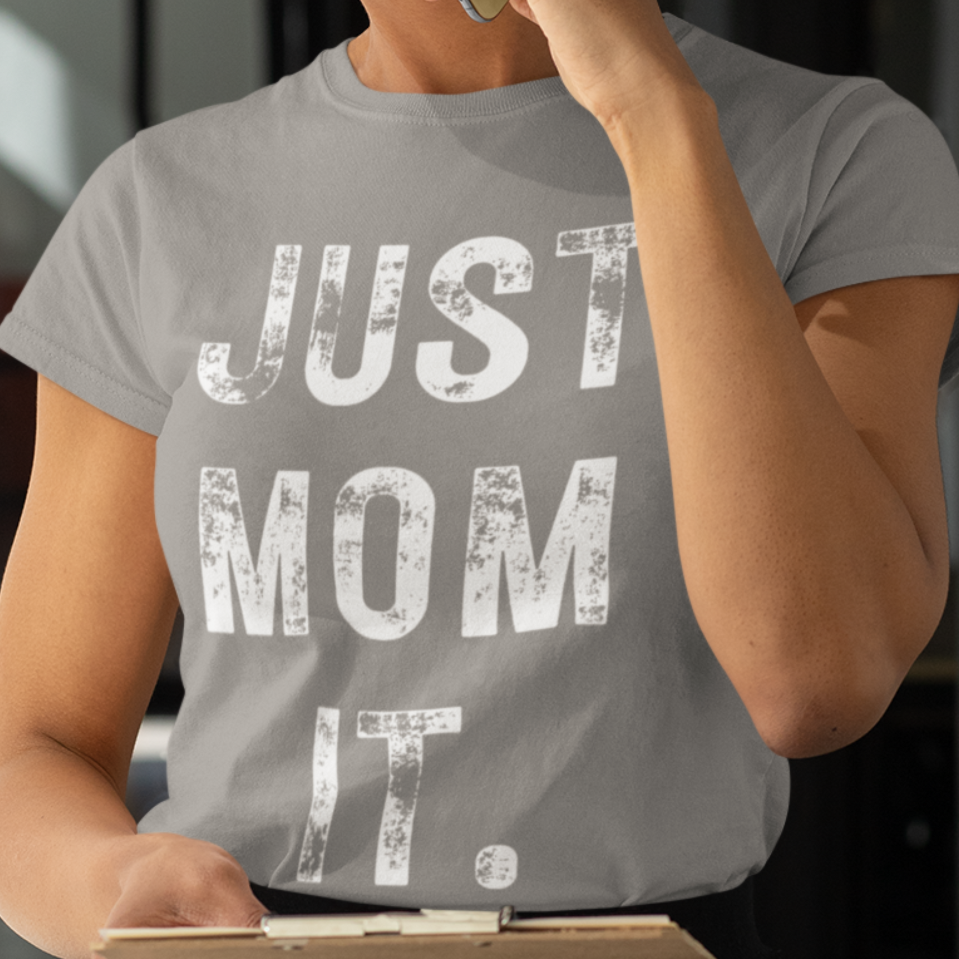 A woman wearing a grey t-shirt featuring bold white text that reads 'UST MOM IT" in a minimalist font.