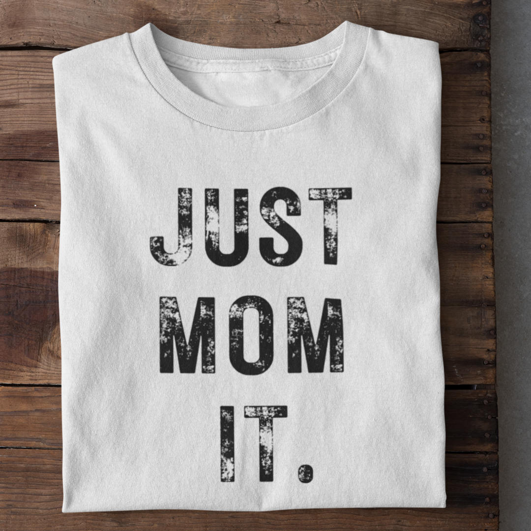 A flat-lay view of a white muscle tank top with black block text reading "JUST MOM IT".