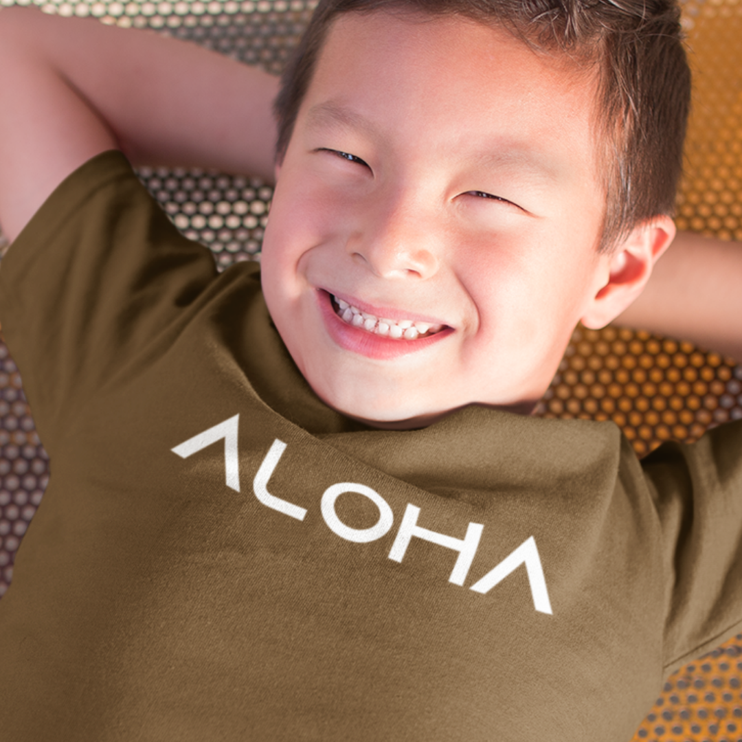 A young boy smiling while wearing a brown minimalist Kids Aloha Shirt from Simply Aloha On The Go.