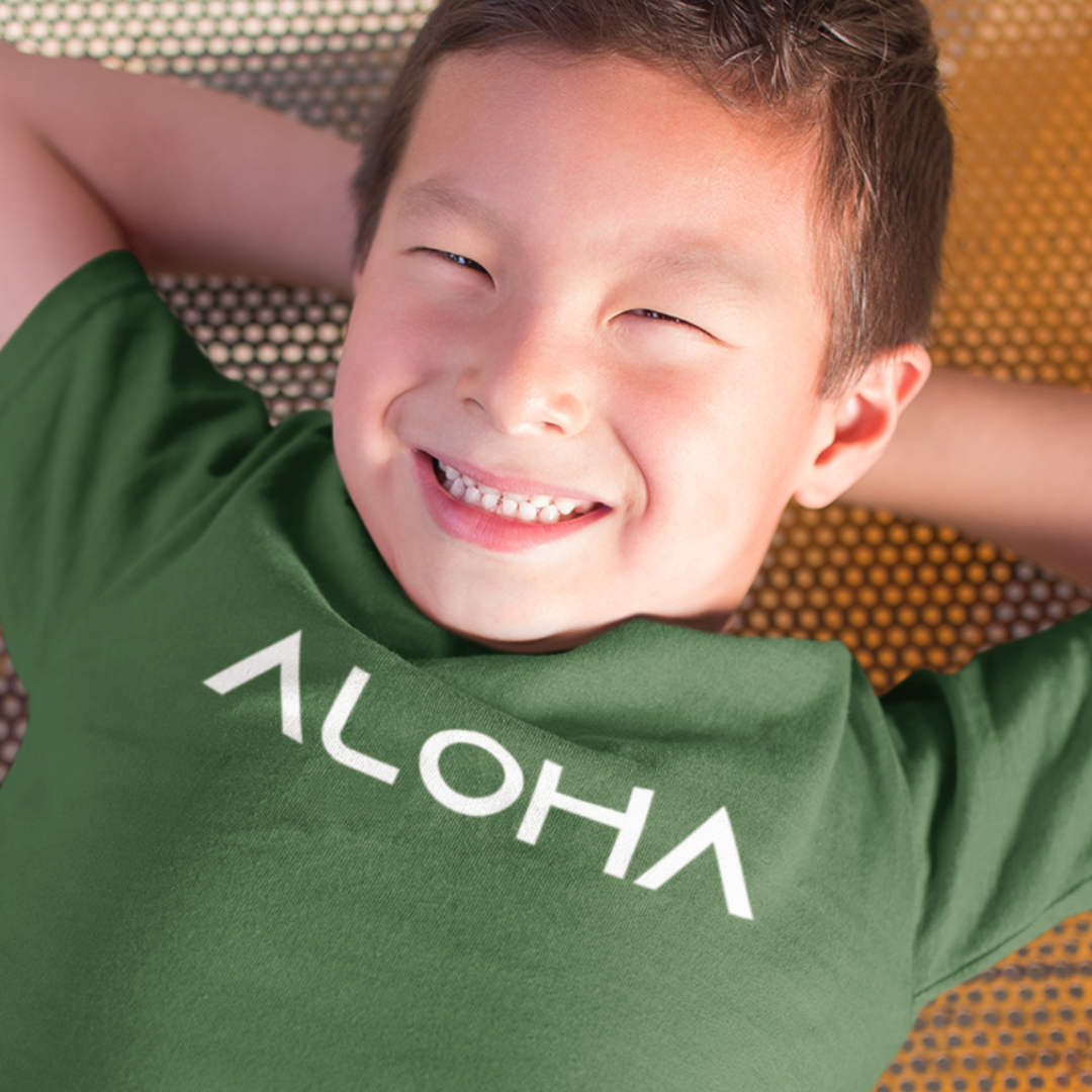A young boy smiling while wearing a green minimalist Kids Aloha Shirt from Simply Aloha On The Go.