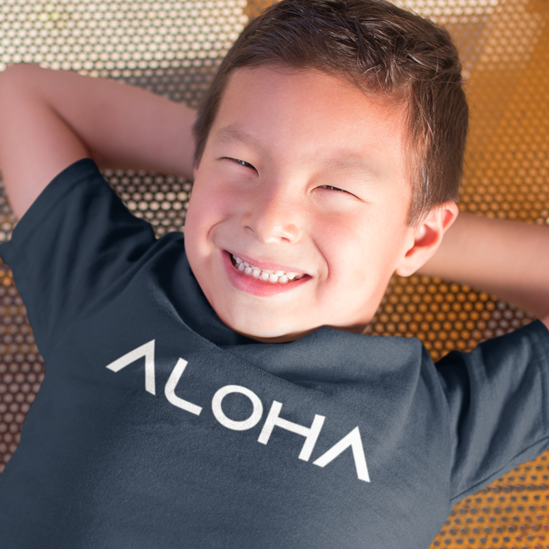 A young boy smiling while wearing a navy blue minimalist Kids Aloha Shirt from Simply Aloha On The Go.