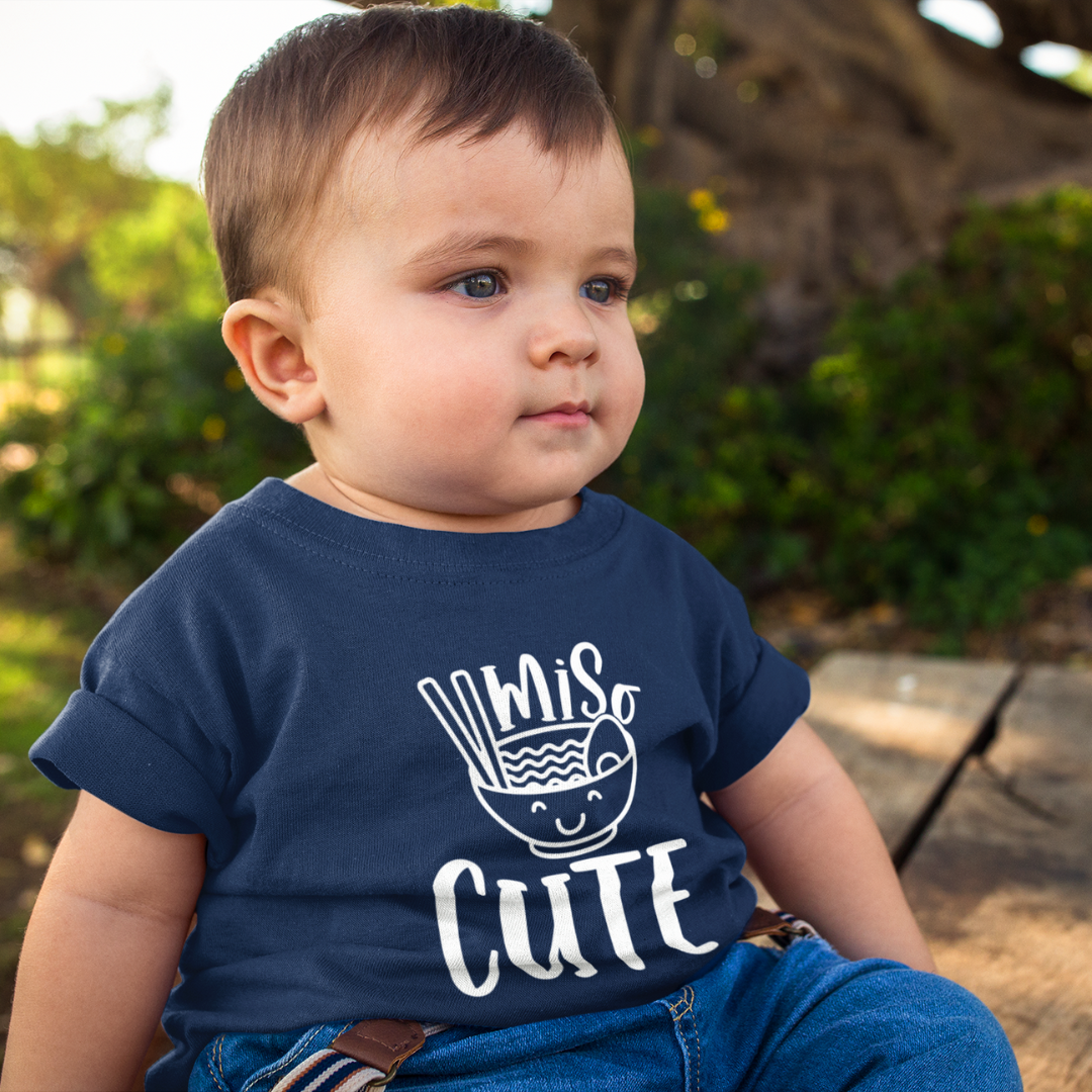 A cute toddler boy wearing a "Miso Cute" T-shirt with a graphic of a smiling bowl of miso soup in a kawaii style. Available in different colors and sizes
