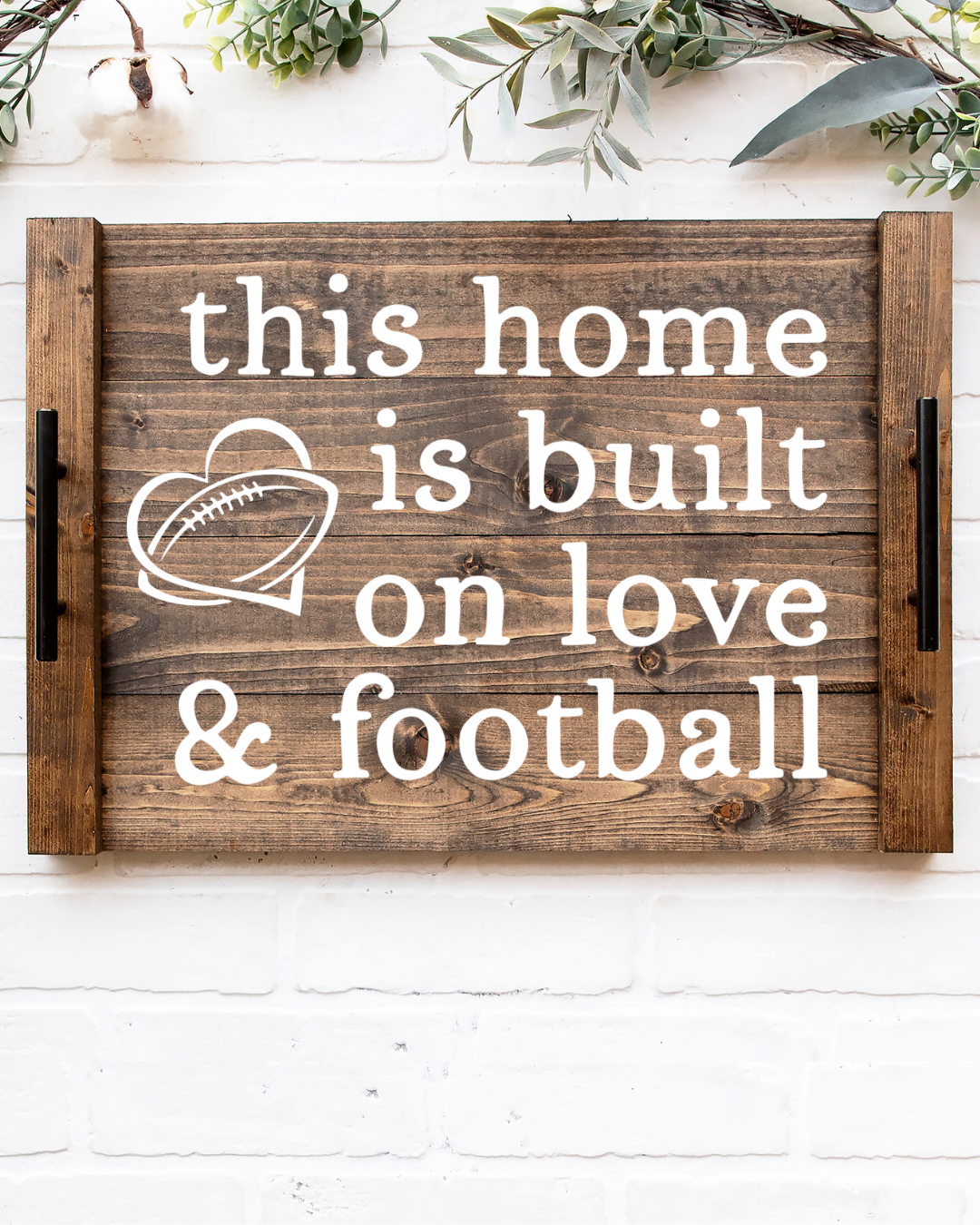 Rustic dark walnut wood noodle board stove cover with white painted text reading this This Home Is Built On Love & Football with a heart graphic and black metal handles
