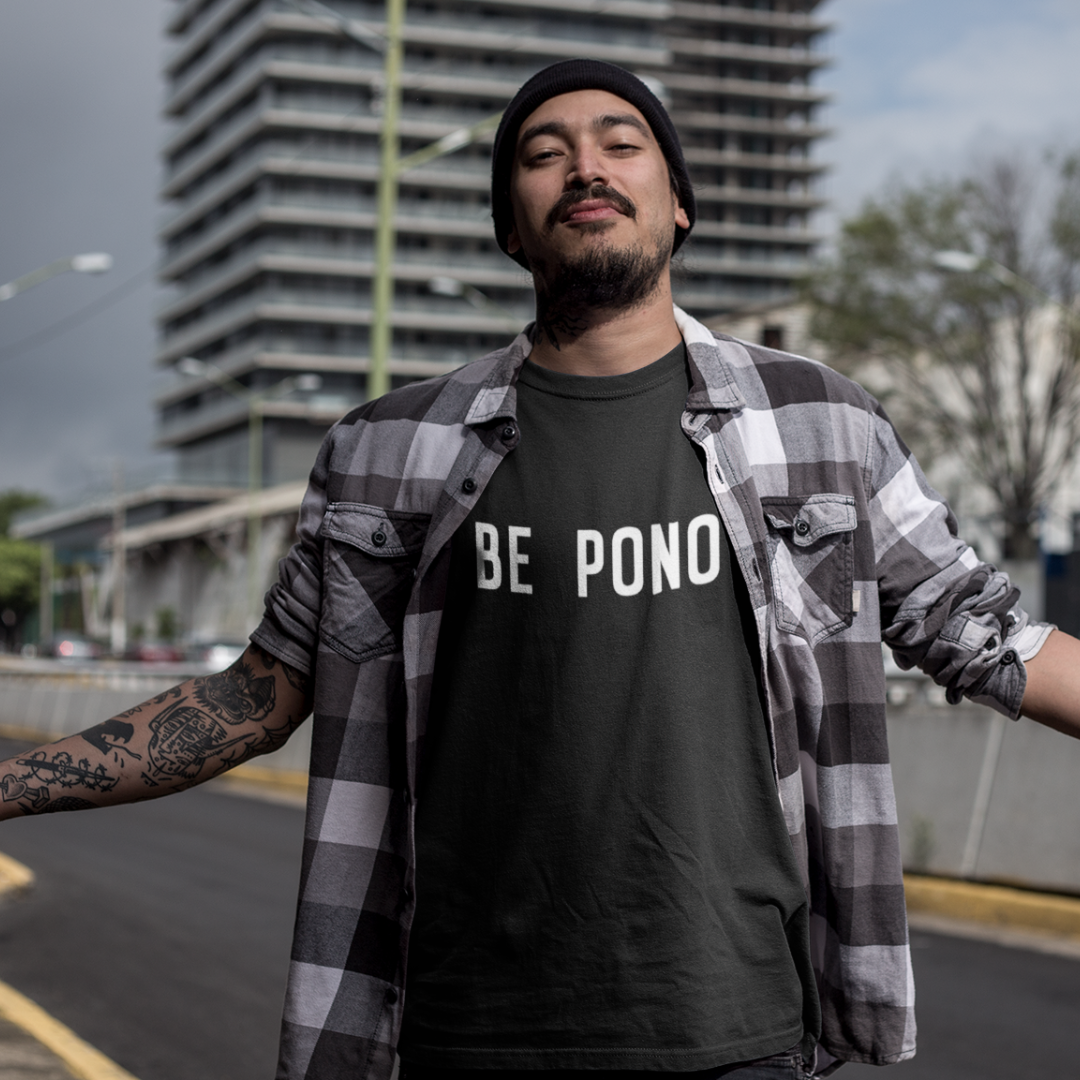 A smiling man wearing a black custom t-shirt with clean whhite text that reads BE PONO