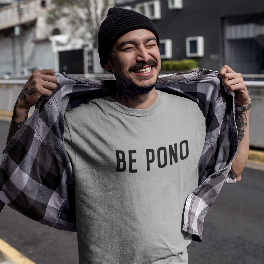 A smiling man with a grey beanie wearing a grey custom t-shirt with clean black text that reads BE PONO