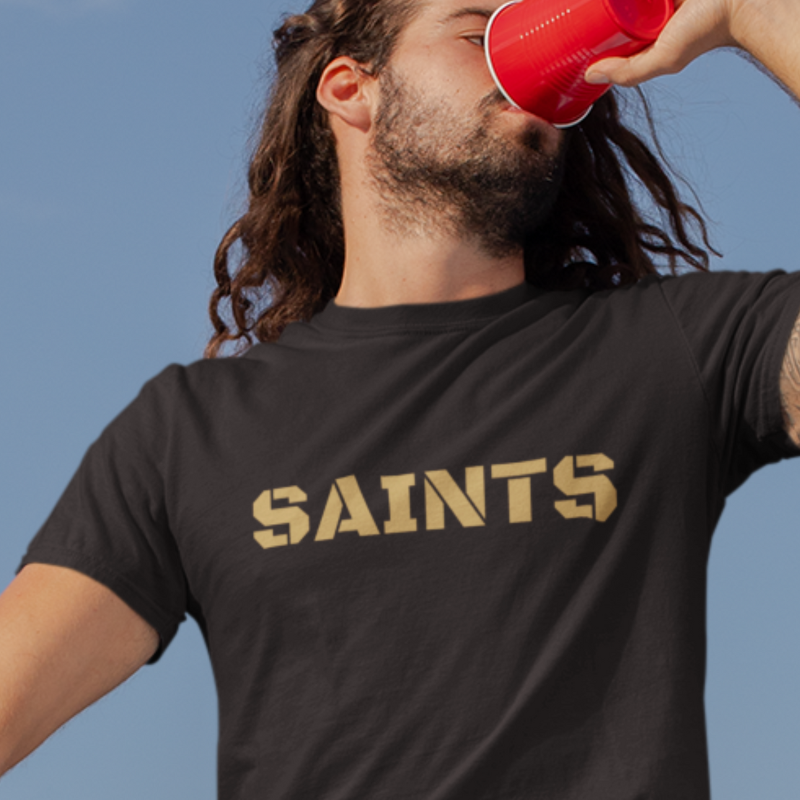 A man at a tailgate wearing a Men’s NFL Game Day T-Shirt printed horizontally with team's name – handcrafted with aloha, SAINTS fan – Simply Aloha On The Go