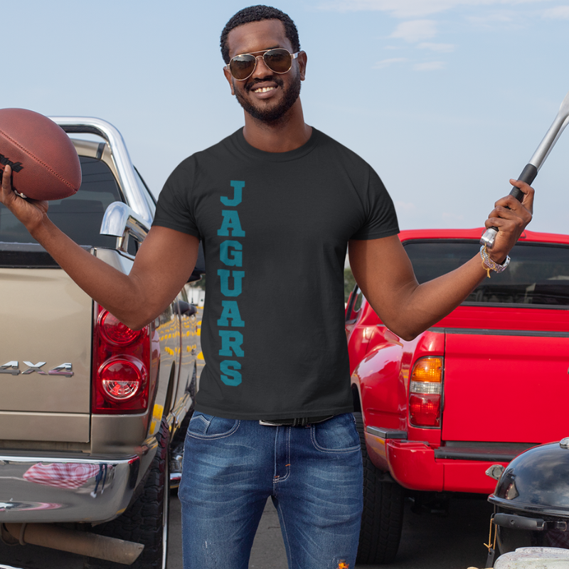 A man at a tailgate party wearing a personalized black men's game day t-shirt featuring vertical teal text reading "Jaguars".
