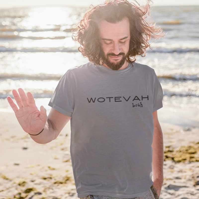 A man wearing a custom grey men's t-shirt that features minimalist black block text reading "WOTEVAH brah"