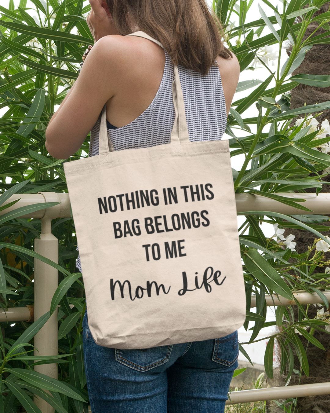 Mom's canvas tote bag featuring text "Nothing in this bag belongs to me, Mom Life" against a green leafy background.