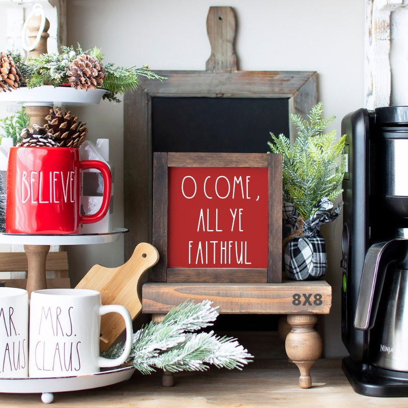 Red O Come All Ye Faithful Christmas sign with white lettering in a rustic wood frame on a holiday shelf display.